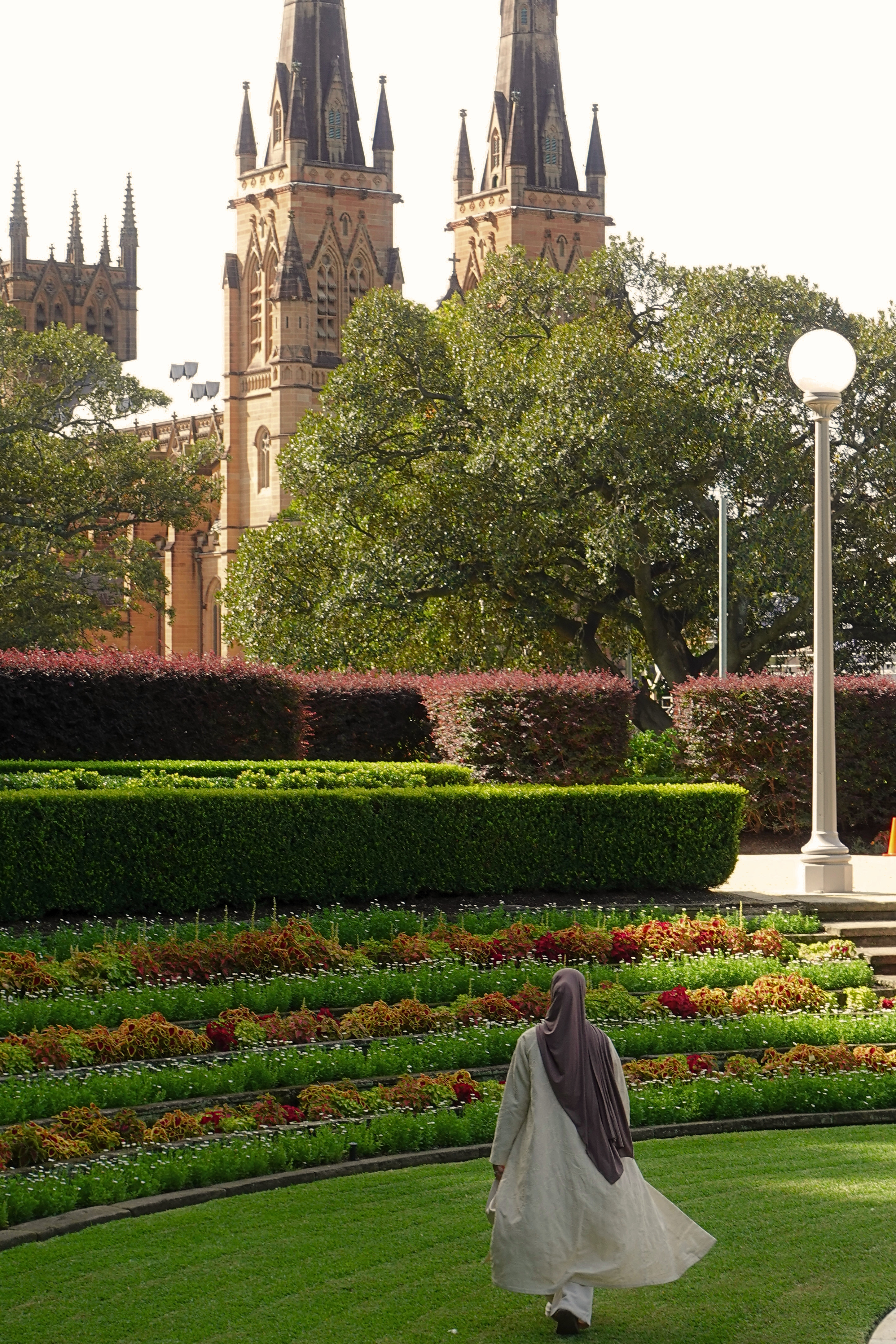 Person in a hijab walking through a garden with a castle in the background